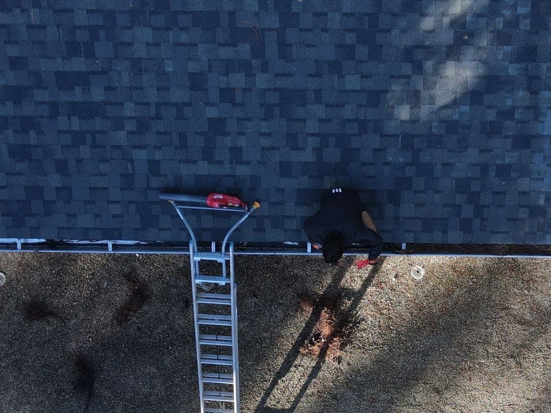 Crew on a ladder clearing a gutter on a shingle roof in Naples